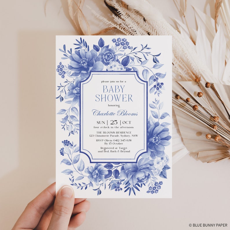 May include: Blue and white floral baby shower invitation with a decorative frame. The invitation reads "Please join us for a Baby Shower honoring Charlotte Blooms" with the date and time of the event, location, RSVP information, and registry details.