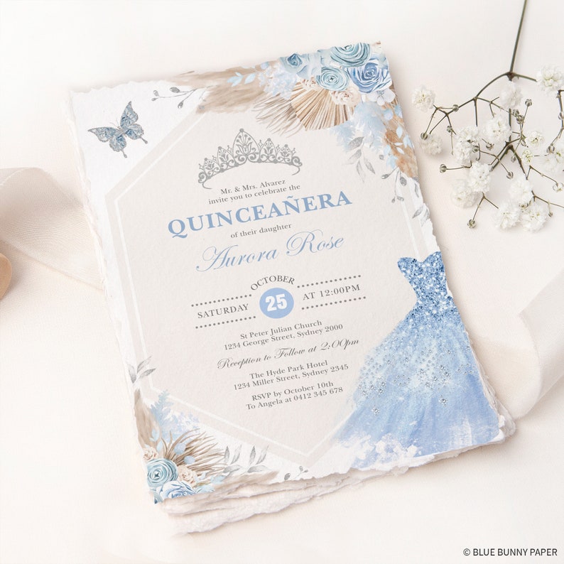 May include: A Quincea&ntilde;era invitation with a blue and white floral design. The invitation features a crown, a butterfly, and a blue dress. The text on the invitation reads "Quincea&ntilde;era" and "Aurora Rose". The date of the event is October 25th.