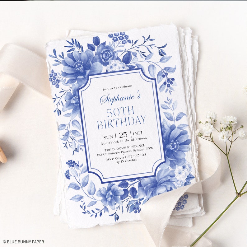 Op de afbeelding: Een blauwe en witte bloemen uitnodiging voor een 50e verjaardag. De uitnodiging heeft een blauw en wit bloemenontwerp met de tekst "Stephanie's 50th Birthday" in een decoratief kader. De uitnodiging bevat ook de datum, tijd en locatie van het feest.