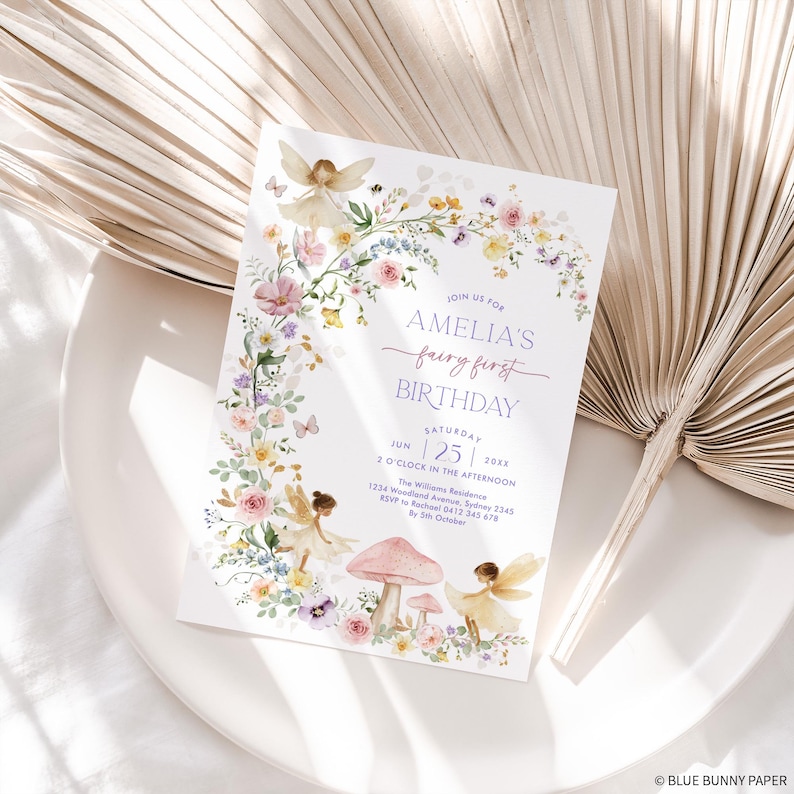 Peut inclure: Une invitation de couleur lilas clair et blanche avec une bordure florale et une illustration de f&eacute;e. Le texte indique "Rejoignez-nous pour le premier anniversaire de f&eacute;e d'Amelia, samedi 25 juin 20XX, 14h00, The Williams Residence, 1234 Woodland Avenue, Sydney 2345, RSVP &agrave; Rachael 0412 245 478 avant le 5 octobre, Blue Bunny Paper".