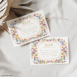 May include: Two white RSVP cards with a floral border and gold accents. The text on the cards reads "RSVP by February 10th, 20XX". The cards have a section for guests to indicate their choice of meal: fish, beef, or vegetarian.