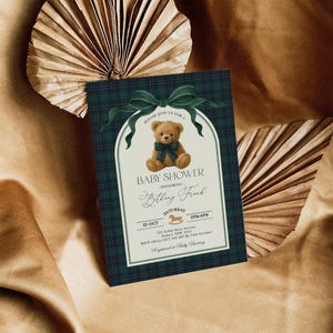 May include: Baby shower invitation with a teddy bear illustration. The invitation features a navy blue plaid background and a cream-colored frame with the text "Baby Shower" and event details. A green bow adorns the top.