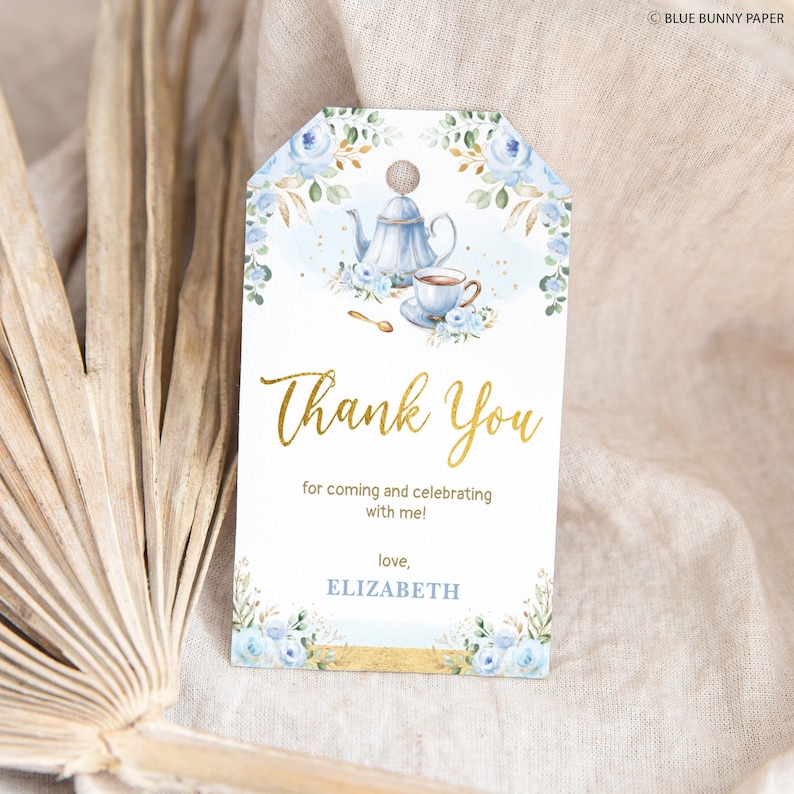 May include: A blue and gold thank you tag with a watercolor illustration of a teapot and teacup. The text reads "Thank You for coming and celebrating with me! love, ELIZABETH".