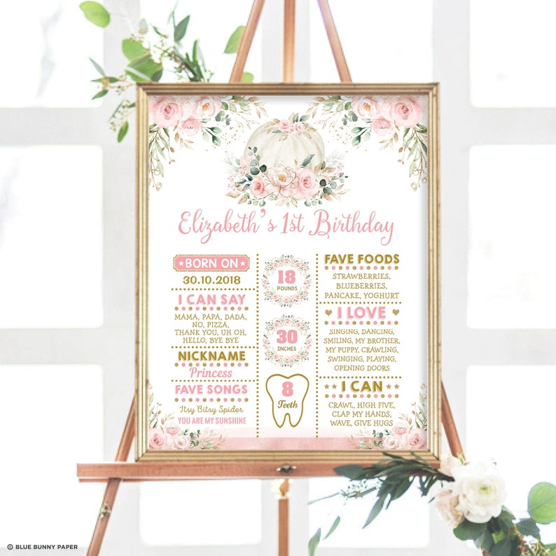 May include: A pink and gold first birthday milestone poster with a pumpkin and floral design. The poster includes the child's name, Elizabeth, and details about their first year, including their weight, height, favorite foods, and things they can do.