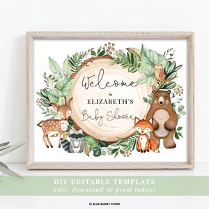 May include: A printable welcome sign for a baby shower with a woodland theme. The sign features a woodgrain circle with a green leafy wreath, a bear, a fox, a deer, a raccoon, and an owl. The text on the sign reads "Welcome to Elizabeth's Baby Shower".