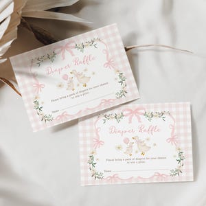 May include: Two baby shower diaper raffle cards. The cards have a pink gingham background and a floral and bow border. The text "Diaper Raffle" is in the center, with a duck and baby duck illustration. The cards read "Please bring a pack of diapers for your chance to win a prize."