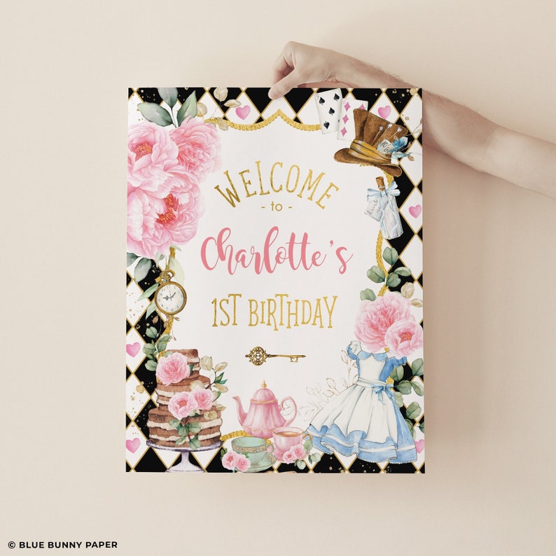 Op de afbeelding: Decoratief bord met de tekst "Welcome to Charlotte's 1st Birthday" in goud en roze. Het bord bevat bloemen en illustraties met het thema Alice in Wonderland, waaronder een taart, theekopjes en een jurk.