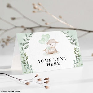 Puede incluir: Una tarjeta de lugar imprimible verde y blanca con una ilustraci&oacute;n de acuarela de un cordero sosteniendo globos verdes. El texto "YOUR TEXT HERE" est&aacute; impreso en negro.