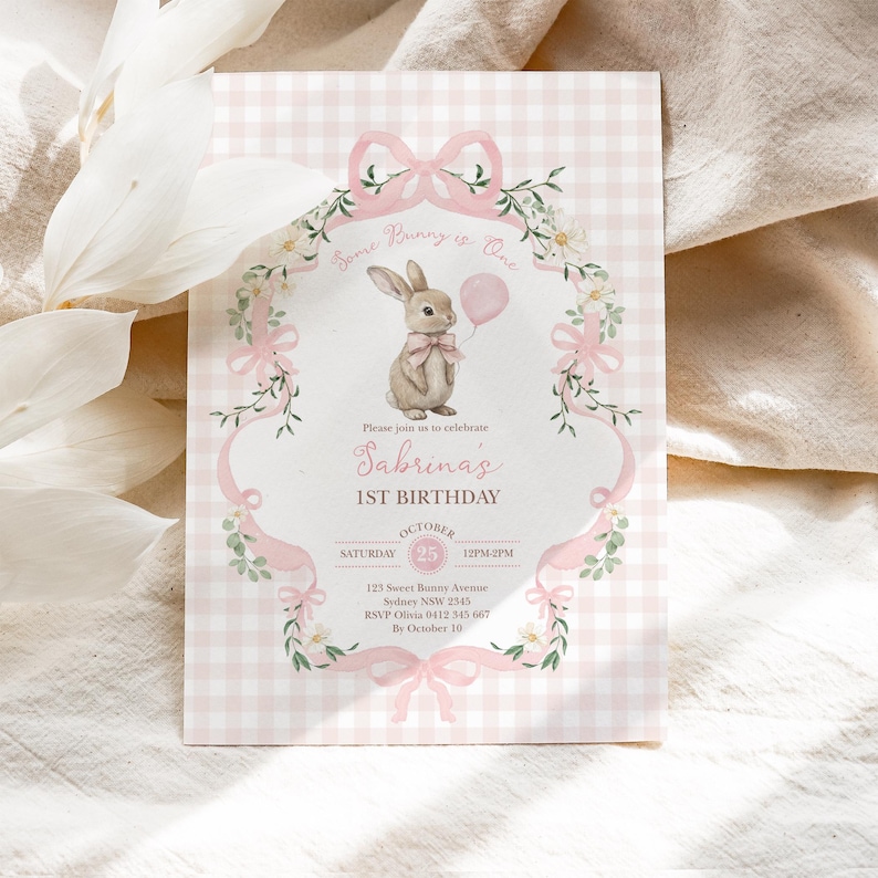 Op de afbeelding: Een roze en witte geruite verjaardagsuitnodiging. De uitnodiging toont een illustratie van een konijn met een roze ballon. De tekst bevat "Some Bunny is One" en "Sabrina's 1e verjaardag".