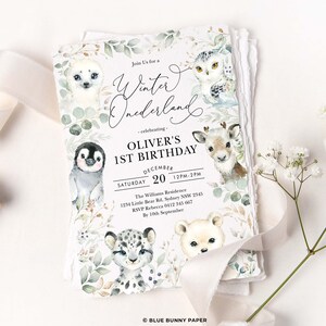 Peut inclure: Une invitation &agrave; un premier anniversaire sur le th&egrave;me du pays des merveilles d'hiver avec une illustration aquarelle d'un pingouin, d'un ours polaire, d'un hibou, d'un phoque et d'un renne. L'invitation comprend le texte "Join Us for a Winter Wonderland - celebrating - Oliver's 1st Birthday December 20 12PM-2PM The Williams Residence 1234 Little Bear Rd, Sydney NSW 2345 RSVP Rebecca 0412 345 667 By 10th September &copy; BLUE BUNNY PAPER".