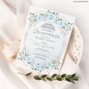 May include: A blue and silver Quincea&ntilde;era invitation with a floral border and a crown. The invitation includes the text "Quincea&ntilde;era" and "Maria Luna" with the date and time of the event.