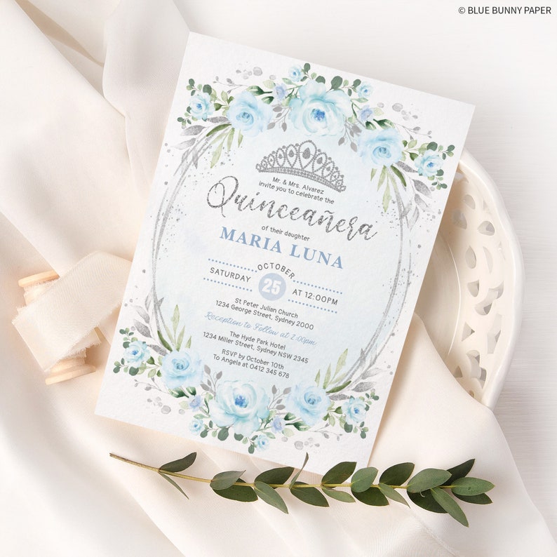 May include: A blue and silver Quincea&ntilde;era invitation with a floral border and a crown. The invitation includes the text "Quincea&ntilde;era" and "Maria Luna" with the date and time of the event.