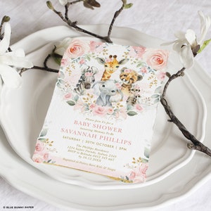 May include: A pink and gold baby shower invitation with a floral wreath and illustrations of a giraffe, zebra, elephant, cheetah, and monkey. The text reads "Please Join Us for a Baby Shower honouring Mommy-To-Be SAVANNAH PHILLIPS Saturday 30th October | 3PM The Phillips Residence 1234 Safari Parade, Sydney 2345 RSVP to Belinda 0412 345 667 by 10.12.20XX Registered at Pottery Barn Kids & Target"