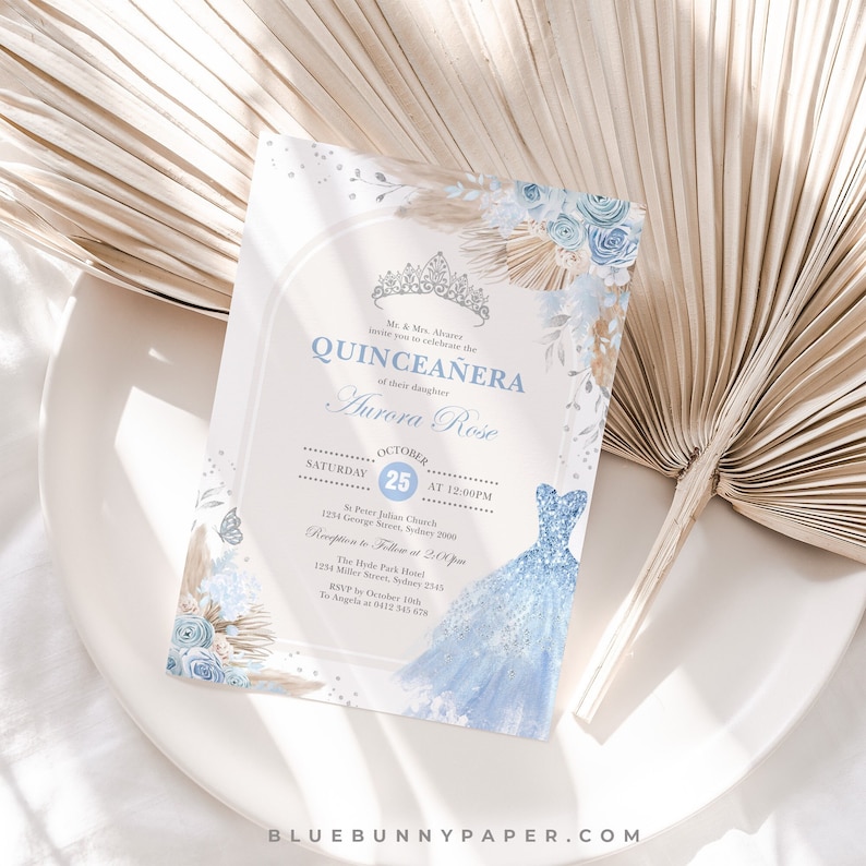 May include: A blue and gold Quincea&ntilde;era invitation with a watercolor illustration of a blue dress and floral accents. The text reads "Mr. & Mrs. Alvarez invite you to celebrate the Quincea&ntilde;era of their daughter Aurora Rose. Saturday, October 25th at 12:00 PM. St. Peter Julian Church, 1234 George Street, Sydney 2000. Reception to follow at 2:00 PM. The Hyde Park Hotel, 1234 Miller Street, Sydney 2743. RSVP by October 15th to Angela at 0412 543 678. BlueBunnyPaper.com"