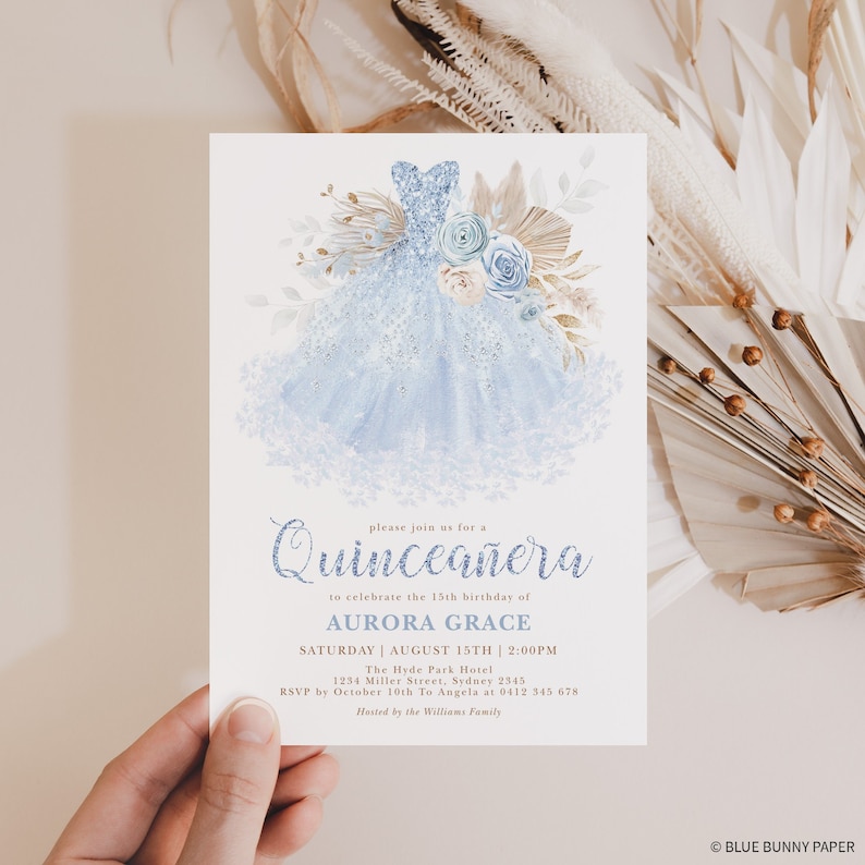 May include: A blue and white quincea&ntilde;era invitation with a watercolor illustration of a blue dress with floral accents. The text reads "Please join us for a Quincea&ntilde;era to celebrate the 15th birthday of Aurora Grace. Saturday, August 15th, 2:00 PM. The Hyde Park Hotel, 1234 Miller Street, Sydney 2345. RSVP by October 10th to Angela at 0412 345 678. Hosted by the Williams Family."