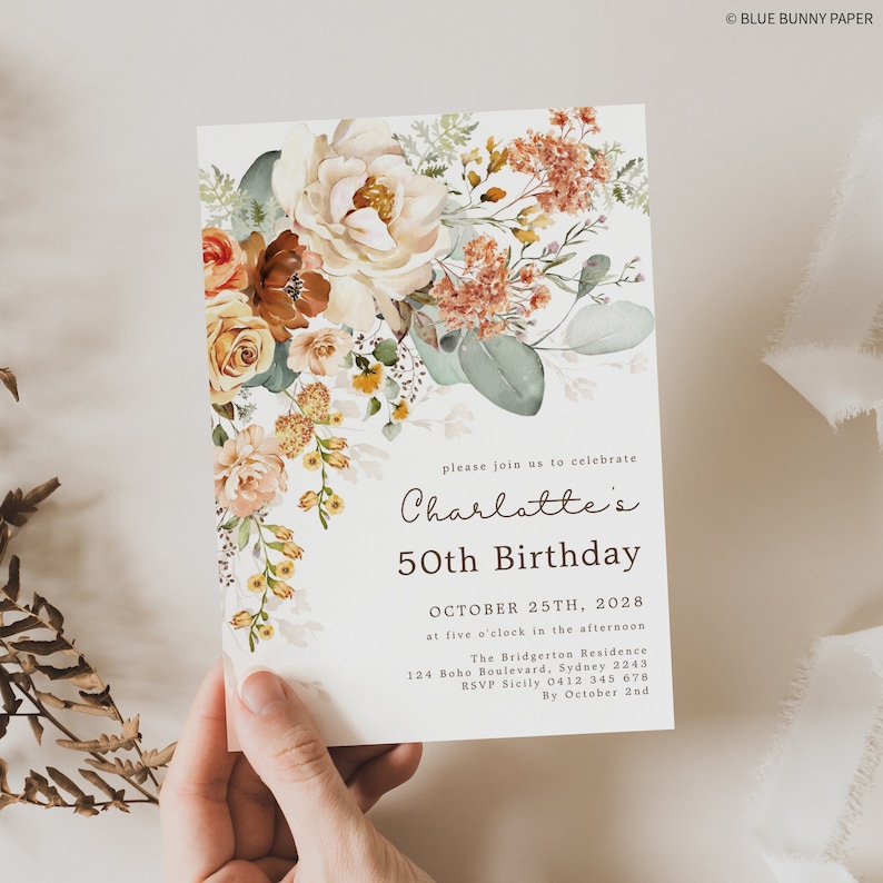 An invitation with a floral design held in one hand.