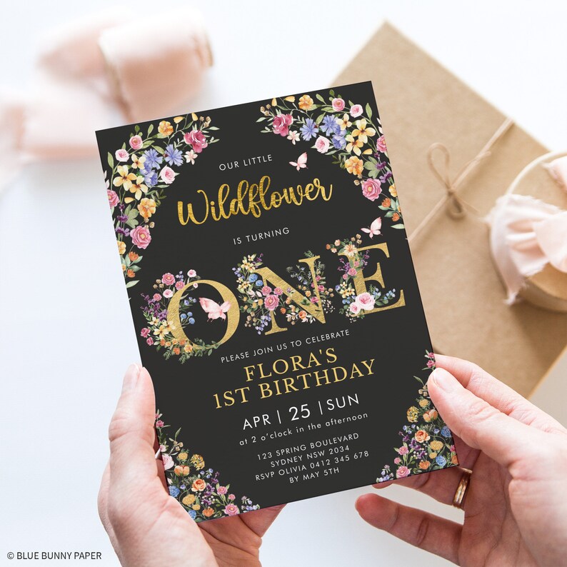 May include: A black and gold floral first birthday invitation for a girl named Flora. The invitation features a gold 'ONE' with floral accents and a butterfly. The text reads 'Our little Wildflower is turning ONE. Please join us to celebrate Flora's 1st Birthday. APR 25 | SUN at 2 o'clock in the afternoon. 123 Spring Boulevard Sydney NSW 2034. RSVP Olivia 0412 345 678 by May 5th.'