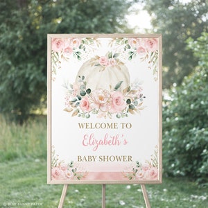 Puede incluir: Un cartel de bienvenida para un baby shower con una calabaza blanca decorada con flores rosas y doradas. El cartel dice "Bienvenido al baby shower de Elizabeth".