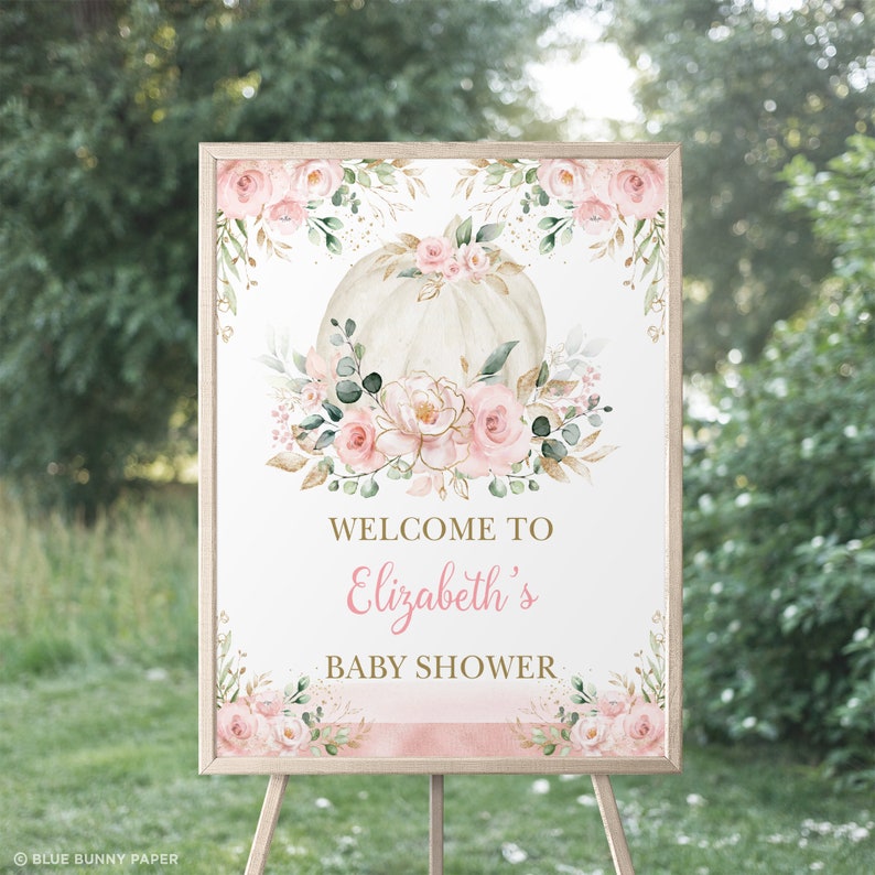 Puede incluir: Un cartel de bienvenida para un baby shower con una calabaza blanca decorada con flores rosas y doradas. El cartel dice "Bienvenido al baby shower de Elizabeth".