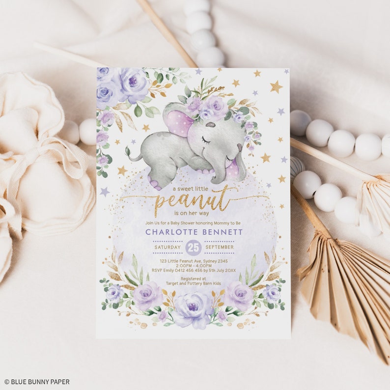 K&ouml;nnte beinhalten: Eine Babyparty-Einladung in lila und gold. Die Einladung zeigt einen niedlichen Elefanten aus der Zeichentrickfigur mit einer rosa Schleife und einem Blumenkranz. Der Text auf der Einladung lautet "a sweet little peanut is on her way" und "Charlotte Bennett".