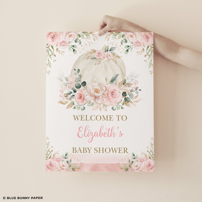 Puede incluir: Una calabaza blanca con detalles florales rosas y dorados, un cartel de bienvenida para el baby shower de Elizabeth.