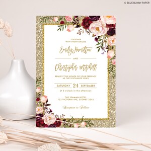 May include: Gold glitter wedding invitation with a burgundy and pink floral design. The invitation reads "Together with their families Emily Hamilton and Christopher Mitchell request the honor of your presence as they exchange vows Saturday 24 September at 5 o'clock in the afternoon The Seaman Hotel 123 Victoria Ave, Sydney 2345 Reception to Follow"