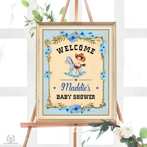 May include: A vintage-style welcome sign for a baby shower. The sign features a blue and white color scheme with a cartoon illustration of a child riding a rocking horse. The text on the sign reads "Welcome to Maddie's Baby Shower".