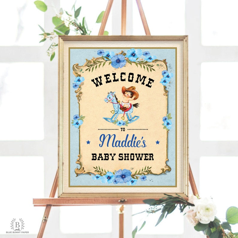 May include: A vintage-style welcome sign for a baby shower. The sign features a blue and white color scheme with a cartoon illustration of a child riding a rocking horse. The text on the sign reads "Welcome to Maddie's Baby Shower".