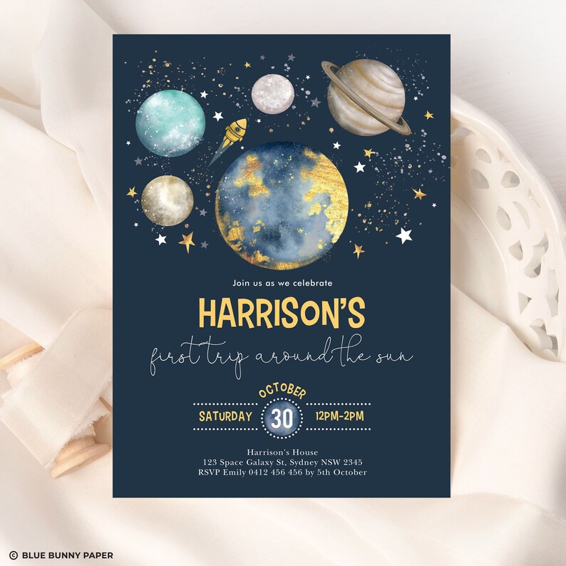 K&ouml;nnte beinhalten: Eine blaue und goldene Partyeinladung zum Thema Weltraum mit dem Text "Join us as we celebrate HARRISON'S first trip around the sun" und Details f&uuml;r eine Party am 30. Oktober von 12:00 bis 14:00 Uhr. Die Einladung zeigt eine Rakete, Planeten und Sterne.