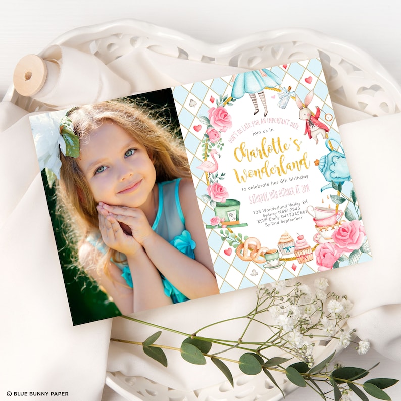 May include: A blue and white invitation with a gold border and a pink and white floral design. The invitation says "Don't be late for an important date, join us in Charlotte's Wonderland to celebrate her 6th birthday, Saturday, 10th October at 3pm, 123 Wonderland Valley Rd, Sydney NSW 2345, RSVP Emily 0412345667 by 2nd September".