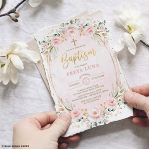 May include: A pink and gold baptism invitation with floral accents. The invitation reads "Join Us to Celebrate the Baptism of our daughter Freya Luna" with the date and time of the event. The invitation also includes the location of the church and the reception.
