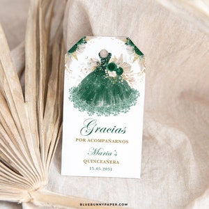 May include: Green and gold thank you tag with a watercolor illustration of a green dress with gold glitter. The text reads "Gracias por acompa&ntilde;arnos Maria's Quincea&ntilde;era 15.05.2031".