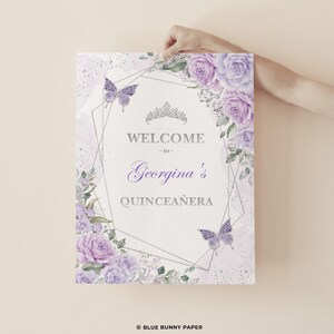 Puede incluir: Un cartel de bienvenida a la Quincea&ntilde;era de color morado y plateado con un marco geom&eacute;trico, detalles florales, mariposas y el texto "Bienvenido a la Quincea&ntilde;era de Georgina".