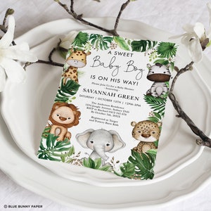 May include: A baby shower invitation with a jungle theme. The invitation features a green, leafy border with a variety of jungle animals, including a giraffe, zebra, lion, elephant, and leopard. The text on the invitation reads "A Sweet Baby Boy Is On His Way!" and includes the name "Savannah Green" and the date and time of the shower.