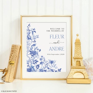 May include: A white wedding sign with blue floral border and text that reads "Welcome to the wedding of Fleur and Andre 10th September 2029".