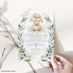 Pu&ograve; includere: Un invito a una festa di benvenuto per un bambino con un'illustrazione ad acquerello di un coniglietto marrone circondato da foglie verdi e glitter dorato. Il testo recita "un piccolo coniglietto &egrave; in arrivo" e include il nome Charlotte Williams, la data e l'ora della festa e la posizione.