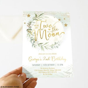 May include: A green and gold invitation for a second birthday party. The invitation features a moon with a gold inscription that reads "Two the Moon". The invitation also includes the text "George's 2nd Birthday" and details about the party, including the date, time, and location.