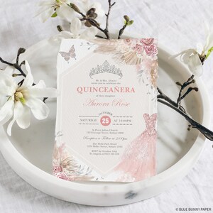 May include: A Quincea&ntilde;era invitation with a pink and white floral design. The invitation features a crown, a dress, and the text "Quincea&ntilde;era" and "Aurora Rose". The date of the event is October 25th.
