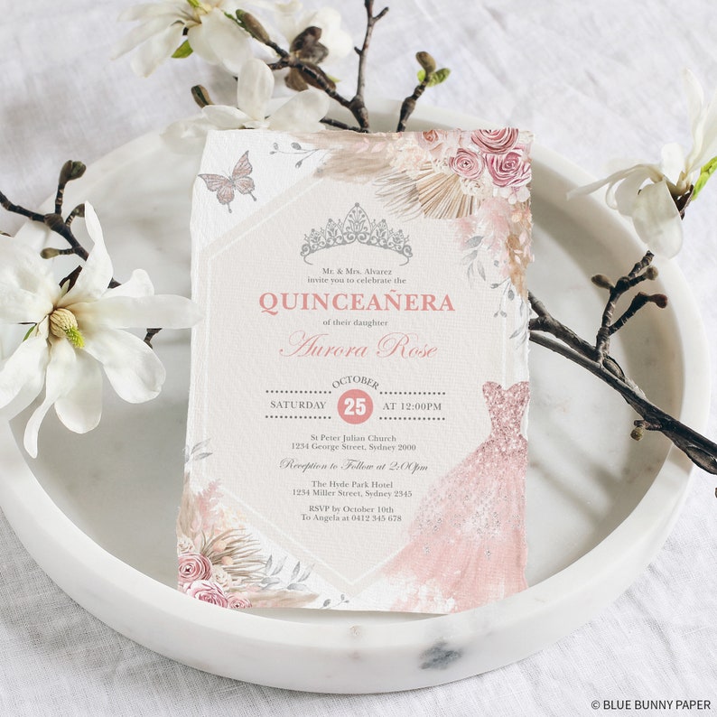 May include: A Quincea&ntilde;era invitation with a pink and white floral design. The invitation features a crown, a dress, and the text "Quincea&ntilde;era" and "Aurora Rose". The date of the event is October 25th.