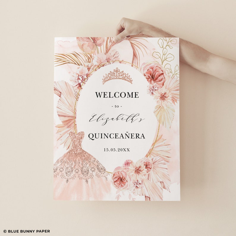 May include: A pink and gold welcome sign for a Quincea&ntilde;era. The sign features a watercolor illustration of a pink dress, flowers, and palm leaves. The text reads "Welcome to Elizabeth's Quincea&ntilde;era 15.05.20XX".