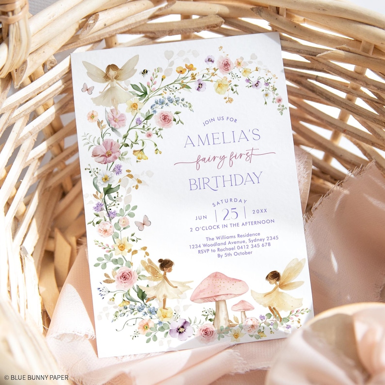 Soft pastel fairy first birthday invitation card. The design features magical fairies in neutral colors and elegant cascading pink and purple florals and greenery.