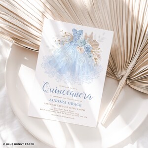 May include: A blue and gold Quincea&ntilde;era invitation with a sparkly blue dress illustration. The invitation text reads "Please join us for a Quincea&ntilde;era to celebrate the 15th birthday of AURORA GRACE SATURDAY | AUGUST 15TH | 2:00PM The Hyde Park Hotel 1234 Miller Street, Sydney 2345 RSVP by October 10th To Angela at 0412 345 678 Hosted by the Williams Family"