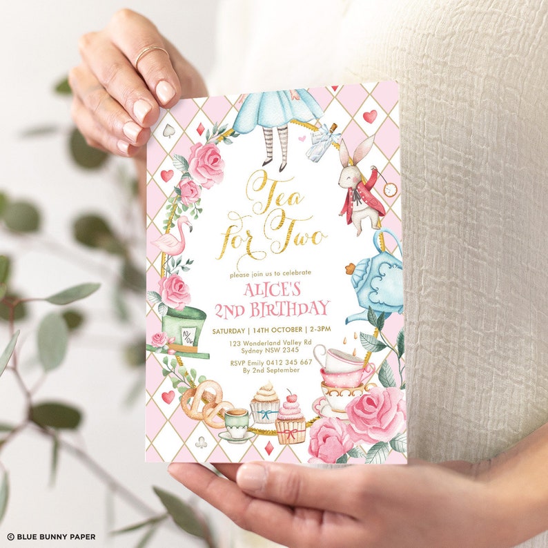 Op de afbeelding: Roze en witte Alice in Wonderland-thema verjaardagsinvitation met gouden letters. De uitnodiging zegt "Tea for Two" en "Alice's 2nd Birthday".