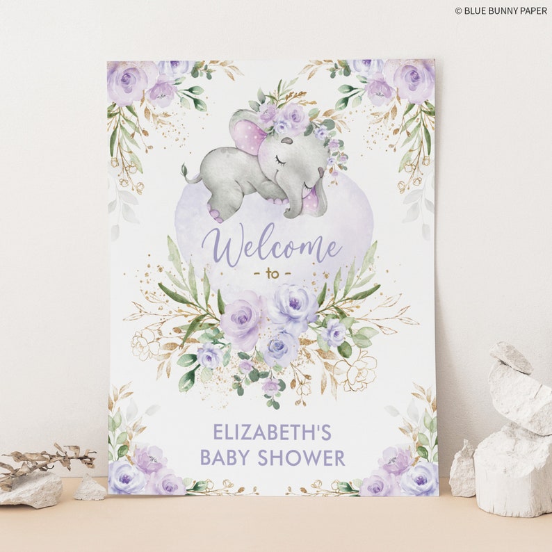 Puede incluir: Un cartel de bienvenida para una baby shower de color morado y dorado con una ilustraci&oacute;n de acuarela de un elefante durmiendo que lleva una corona de flores. El cartel dice "Bienvenido a la baby shower de Elizabeth".