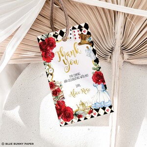May include: A white thank you tag with gold lettering and red roses. The tag features a black and white chequered pattern and illustrations of Alice in Wonderland characters. The text reads "Thank You" and "For coming and celebrating with me! Love, Alice Rose."