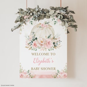 Puede incluir: Un cartel de bienvenida para un baby shower con una calabaza blanca decorada con flores rosas y doradas. El cartel dice "Bienvenido al baby shower de Elizabeth".