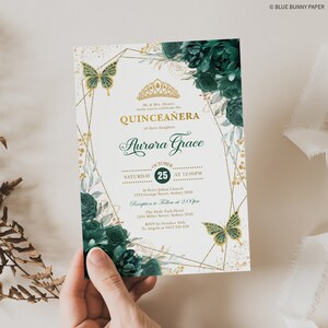 K&ouml;nnte beinhalten: Eine Quincea&ntilde;era-Einladung mit goldfarbenem und wei&szlig;em Hintergrund. Die Einladung zeigt eine goldene Krone, Schmetterlinge und gr&uuml;ne Blumenmuster. Der Text auf der Einladung lautet "Quincea&ntilde;era" und "Aurora Grace".