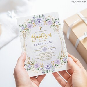 May include: A baptism invitation with a watercolor floral design in shades of purple and green. The invitation features a gold cross and the text "Baptism" in gold lettering. The invitation also includes the name "FREYA LUNA" and the date and time of the baptism. The invitation is decorated with gold glitter.