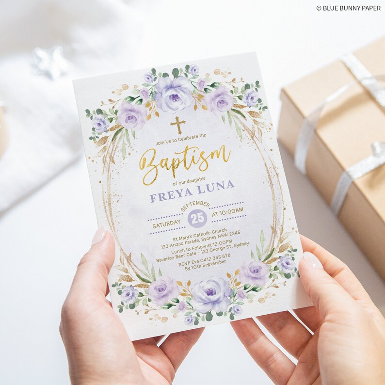 May include: A baptism invitation with a watercolor floral design in shades of purple and green. The invitation features a gold cross and the text "Baptism" in gold lettering. The invitation also includes the name "FREYA LUNA" and the date and time of the baptism. The invitation is decorated with gold glitter.