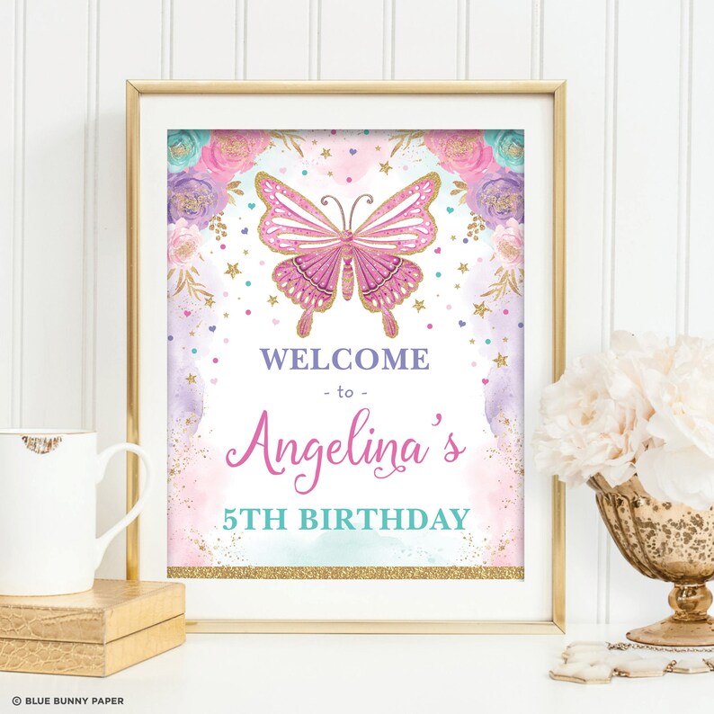 May include: A pink and gold welcome sign with a butterfly and flowers. The sign says "Welcome to Angelina's 5th Birthday".